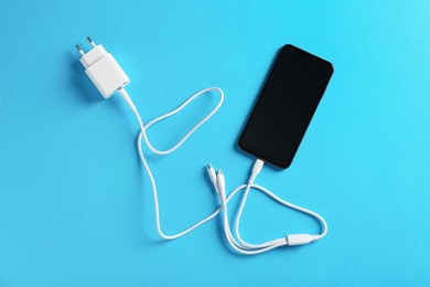 Photo of Triple charge cable connected to smartphone on light blue background, top view