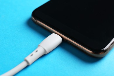 Photo of USB charge cable connected to smartphone on light blue background, closeup