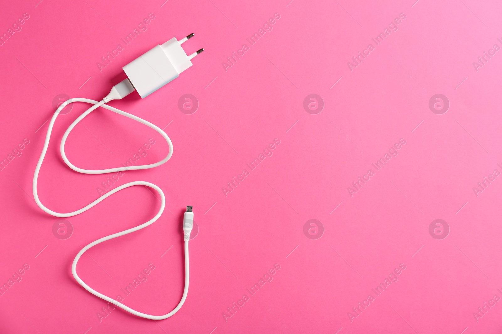 Photo of USB power adapter with charge cable on pink background, top view. Space for text