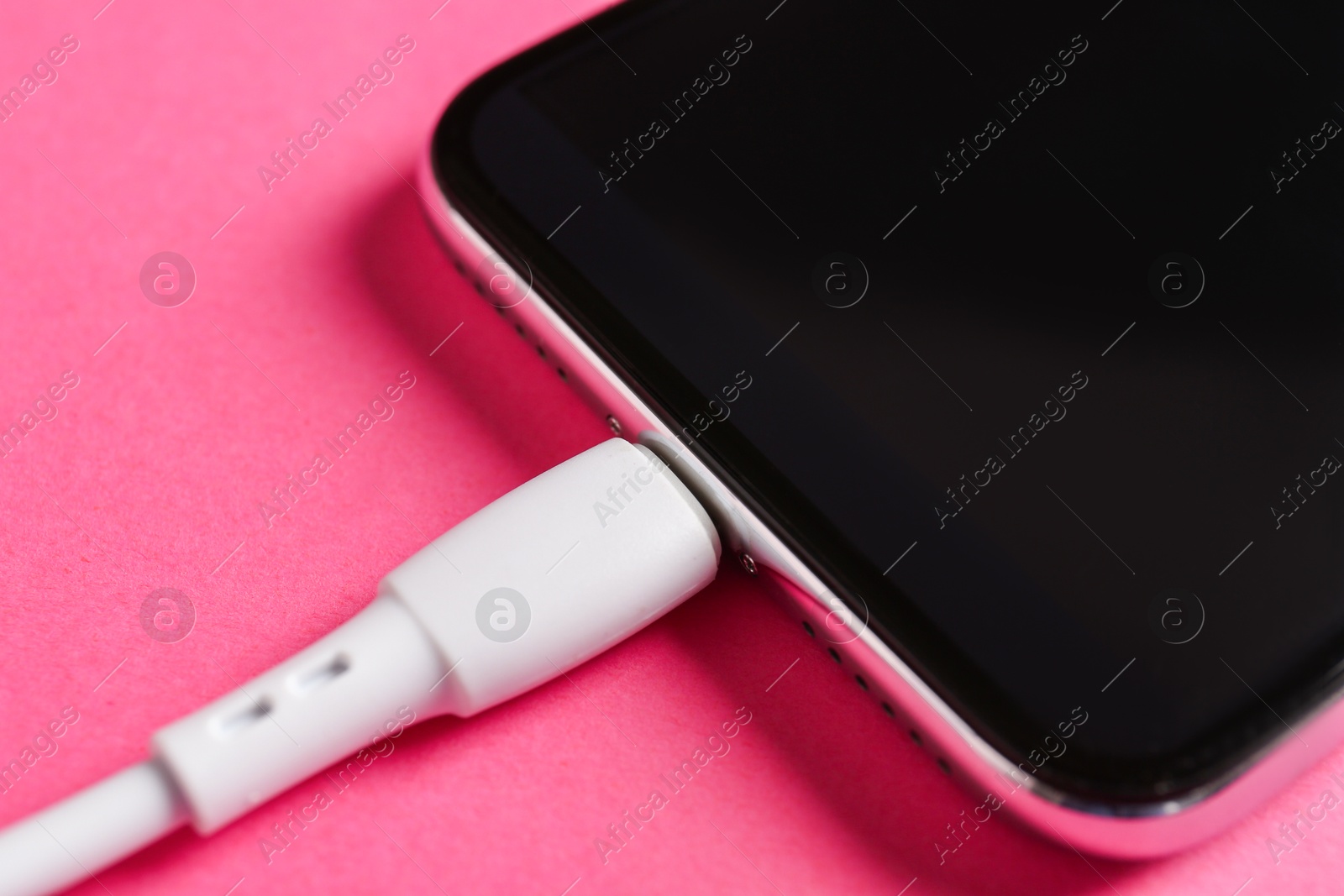 Photo of USB charge cable connected to smartphone on pink background, closeup