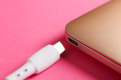 Photo of USB charge cable and laptop on pink background, closeup