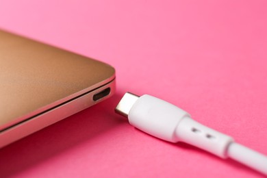 Photo of USB charge cable and laptop on pink background, closeup