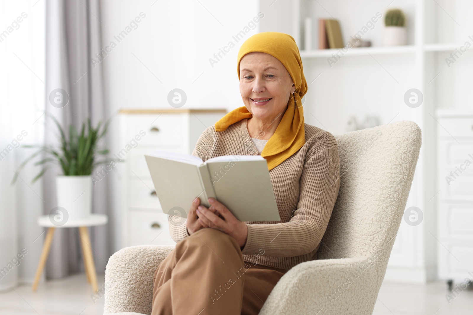 Photo of Senior woman with cancer reading book on armchair at home