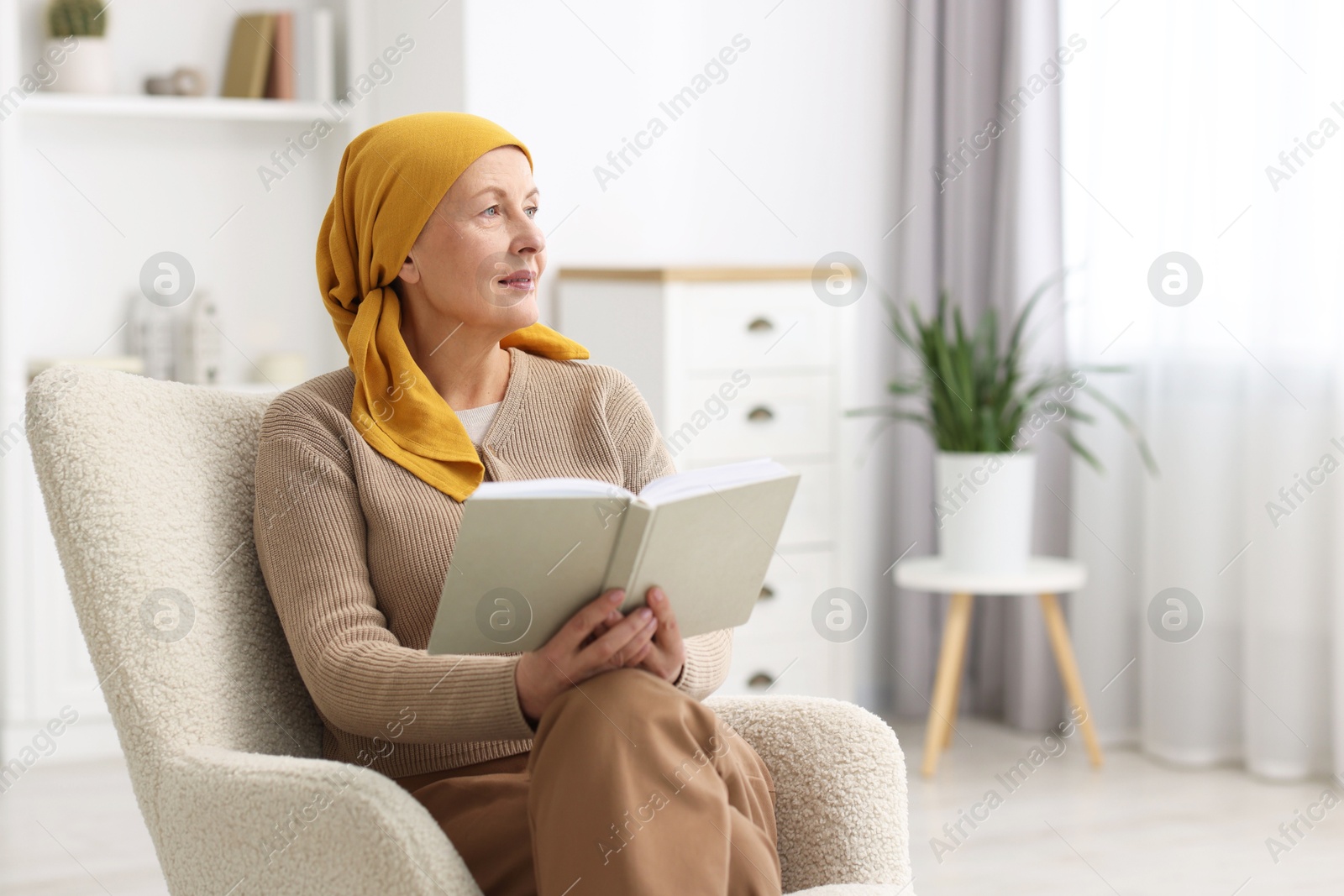 Photo of Senior woman with cancer reading book on armchair at home