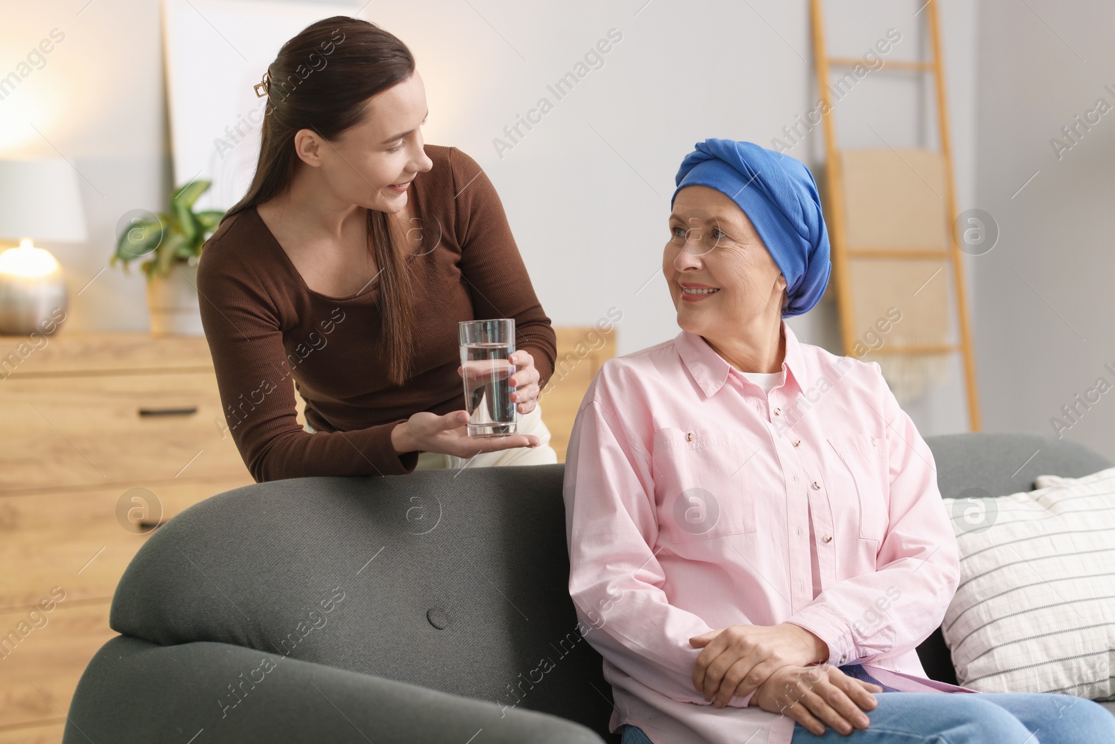 Photo of Caregiver giving water to woman with cancer indoors