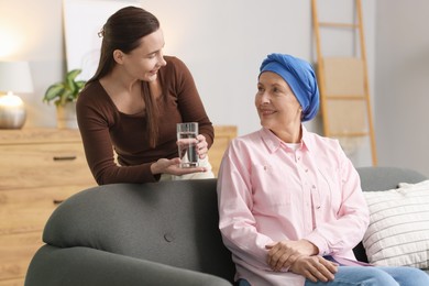 Caregiver giving water to woman with cancer indoors