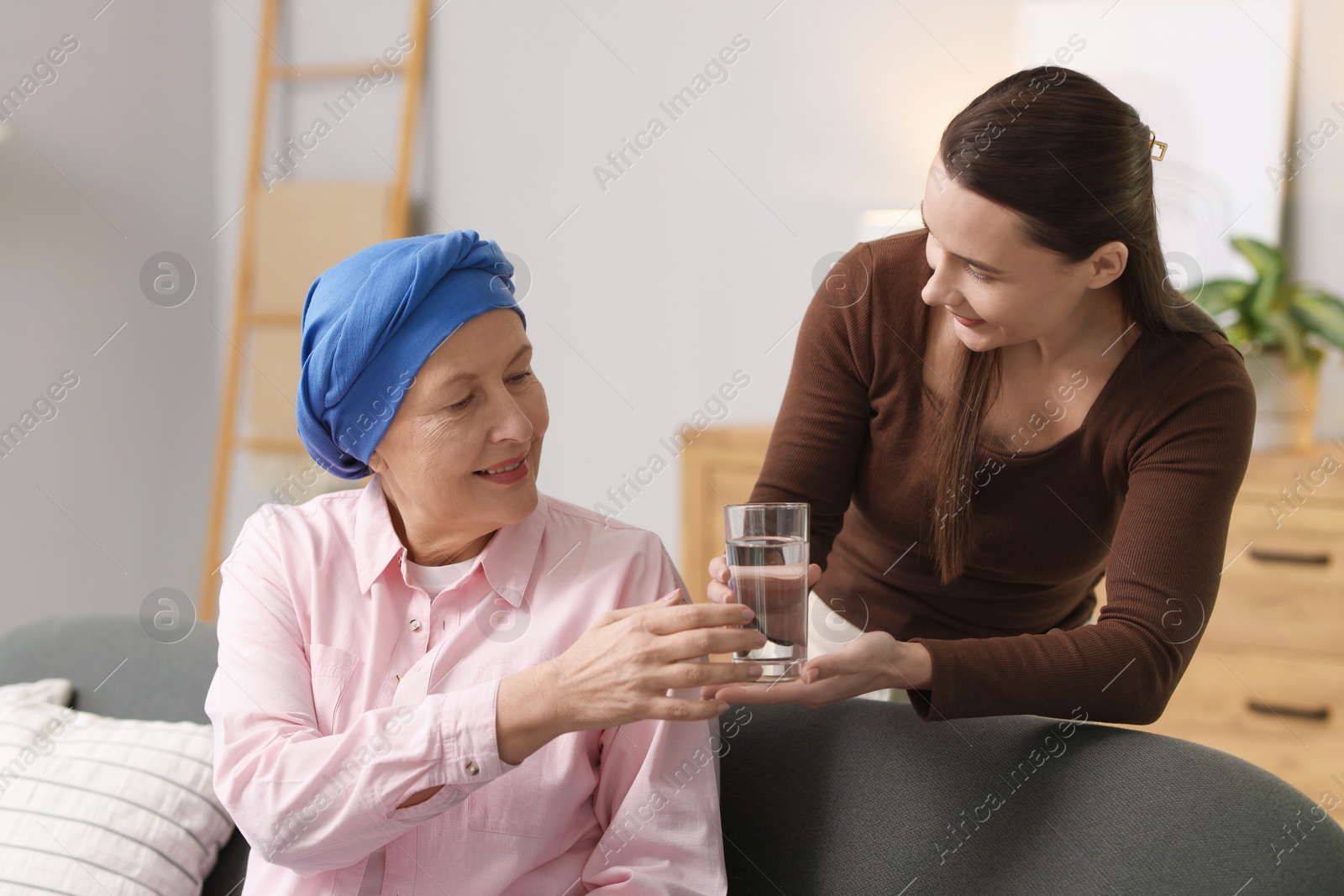 Photo of Caregiver giving water to woman with cancer indoors