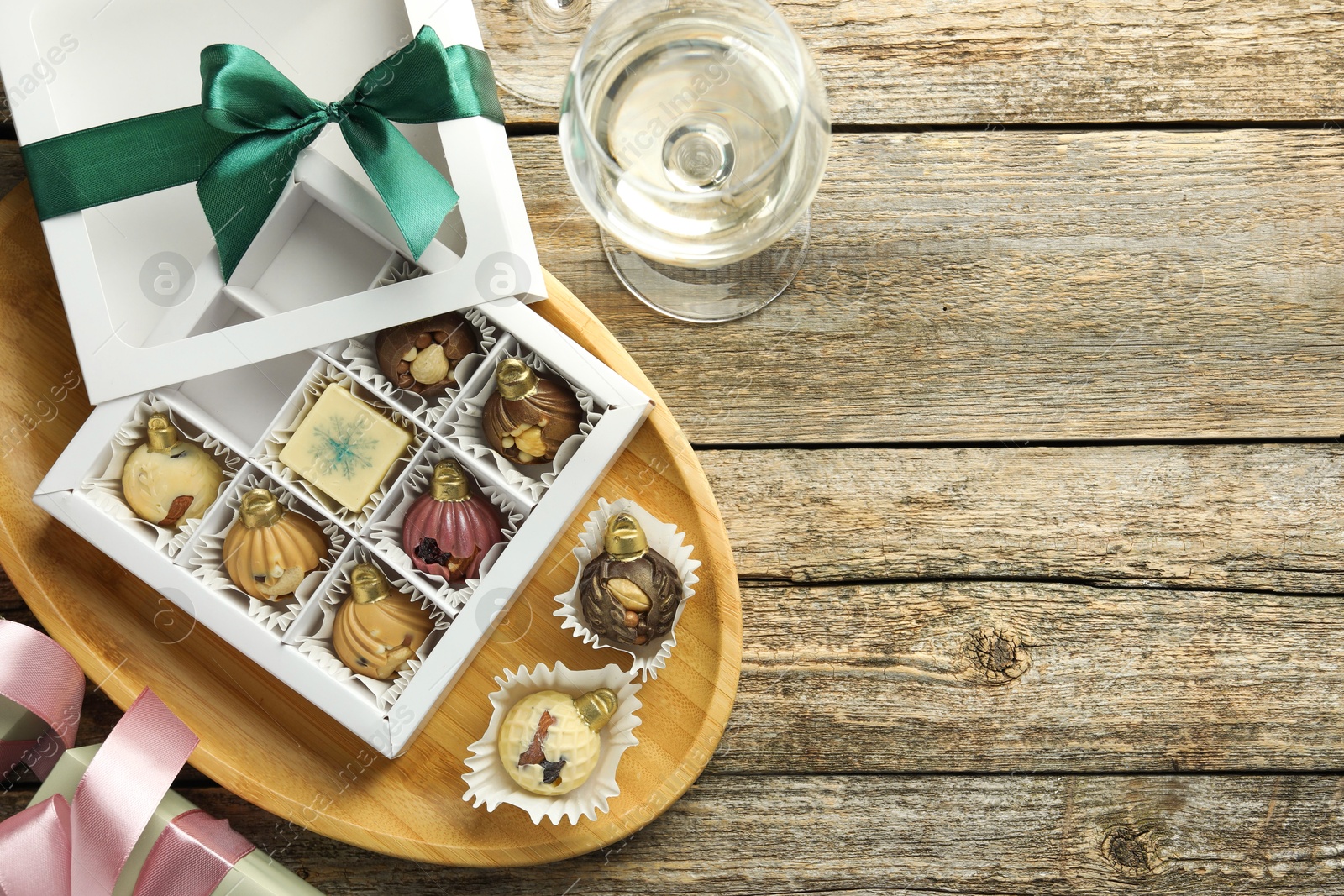 Photo of Box with tasty sweets in shape of baubles and wine on wooden background, flat lay. Space for text