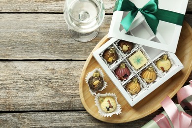 Photo of Box with tasty sweets in shape of baubles and wine on wooden background, flat lay. Space for text