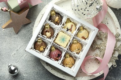 Photo of Box with tasty sweets in shape of baubles and Christmas decor on grey background, flat lay