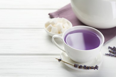 Photo of Aromatic lavender tea in cup, sugar cubes and dry flowers on white wooden table, closeup. Space for text