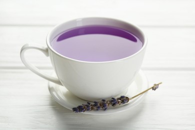 Photo of Aromatic lavender tea in cup and dry flowers on white wooden table, closeup