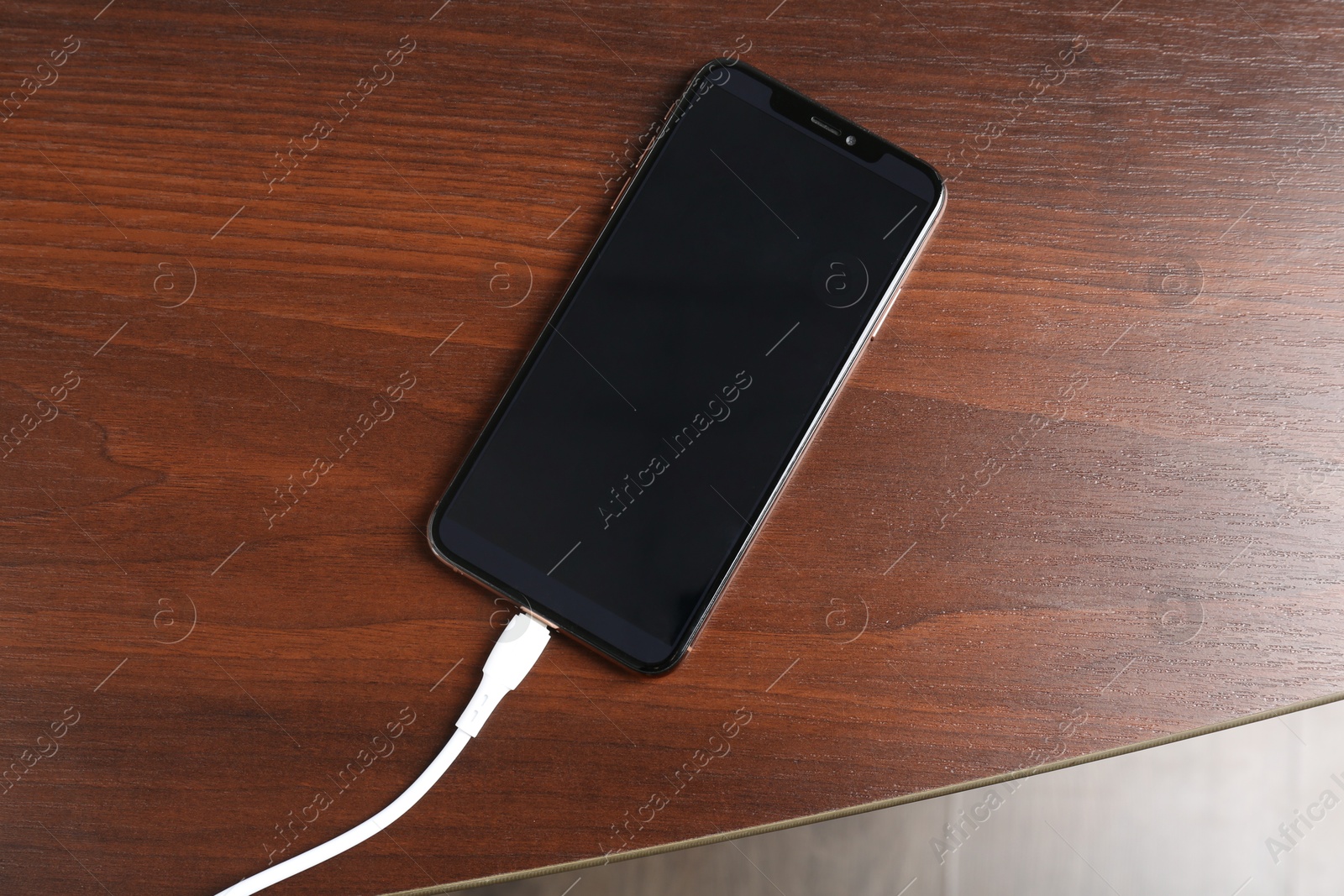 Photo of Smartphone charging from cable on wooden table, top view