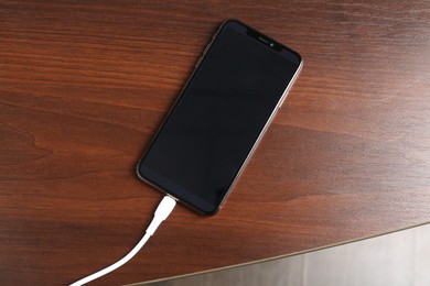 Photo of Smartphone charging from cable on wooden table, top view