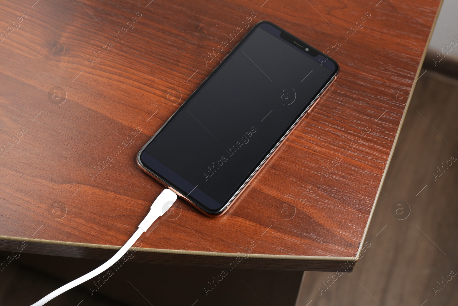 Photo of Smartphone charging from cable on wooden table, above view