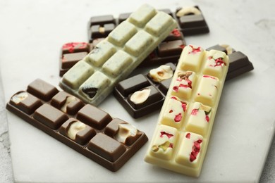 Delicious chocolate bars with different flavors on light table, closeup