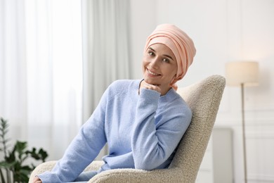 Photo of Portrait of smiling woman with cancer in headscarf on armchair indoors