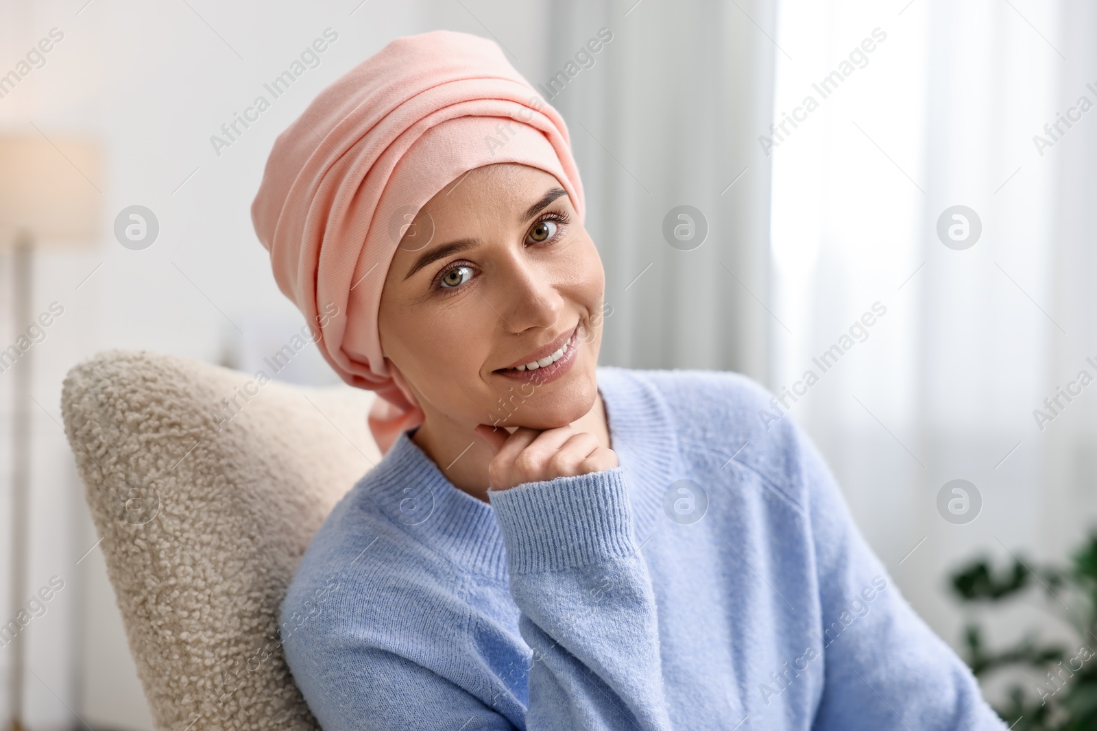 Photo of Portrait of smiling woman with cancer in headscarf on armchair indoors