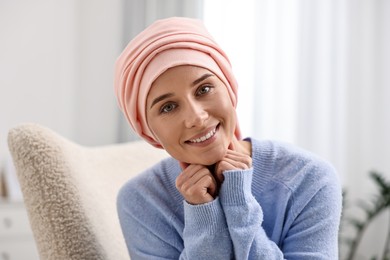 Photo of Portrait of smiling woman with cancer in headscarf on armchair indoors