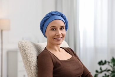 Photo of Portrait of smiling woman with cancer in headscarf on armchair indoors