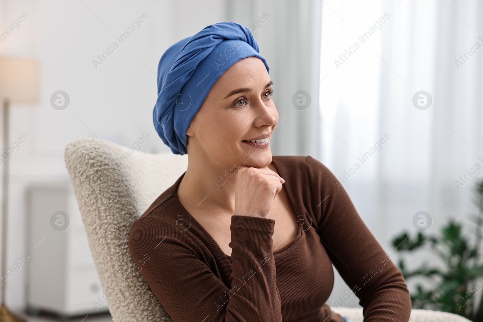 Photo of Portrait of smiling woman with cancer in headscarf on armchair indoors