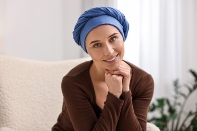 Photo of Portrait of smiling woman with cancer in headscarf on armchair indoors