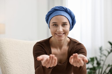 Photo of Portrait of smiling woman with cancer in headscarf on armchair indoors