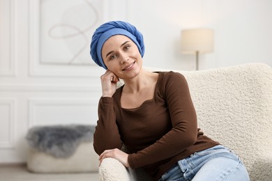 Portrait of smiling woman with cancer in headscarf on armchair indoors. Space for text