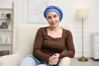 Photo of Portrait of smiling woman with cancer in headscarf on armchair indoors