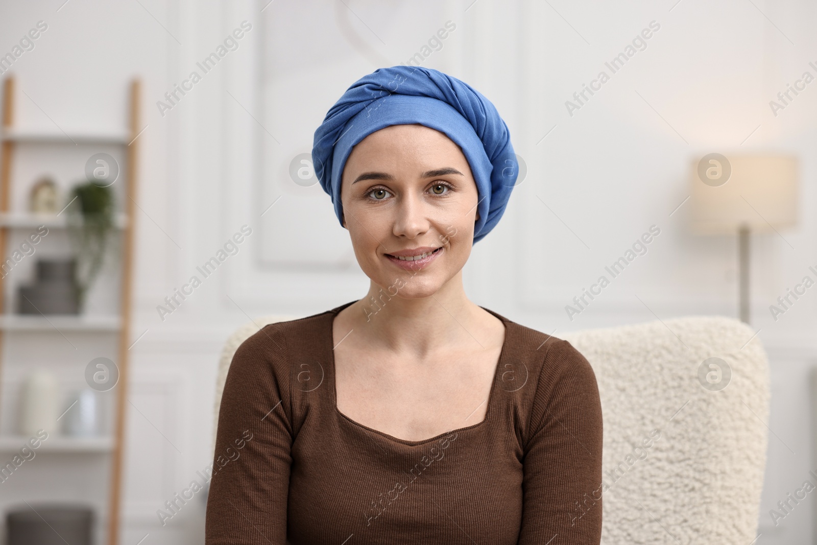 Photo of Portrait of smiling woman with cancer in headscarf on armchair indoors