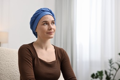 Young woman with cancer in headscarf on armchair indoors. Space for text