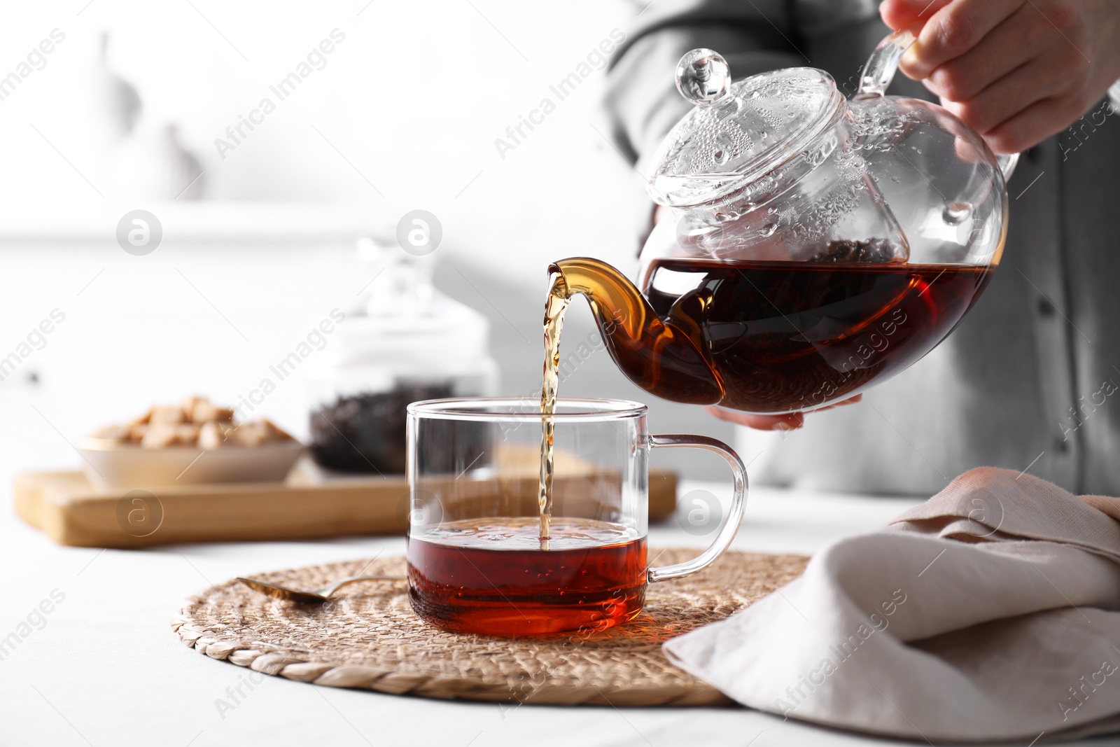 Photo of Woman pouring hot black tea into cup at white table, closeup