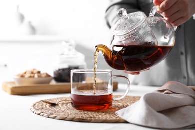 Photo of Woman pouring hot black tea into cup at white table, closeup