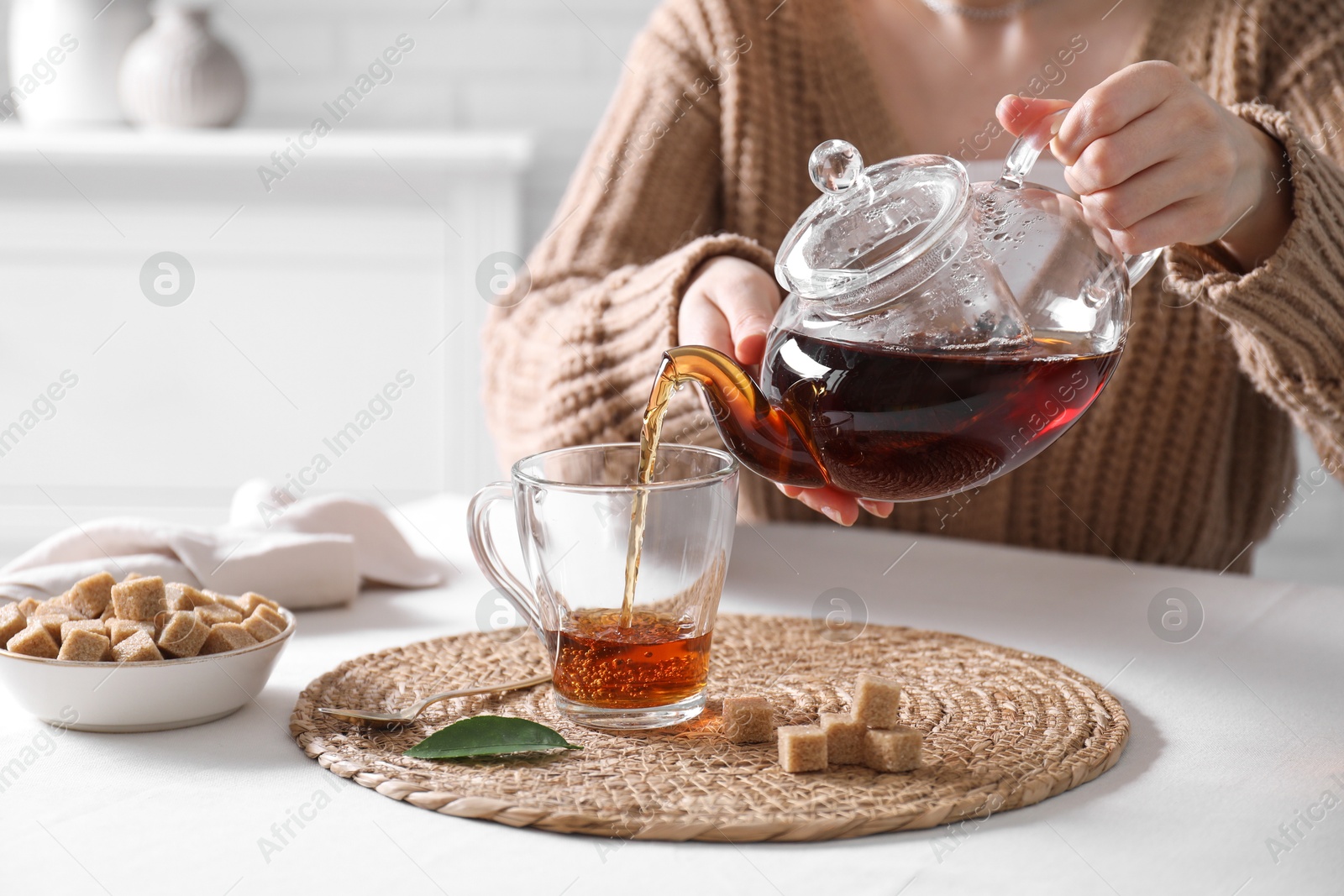 Photo of Woman pouring hot black tea into cup at white table, closeup