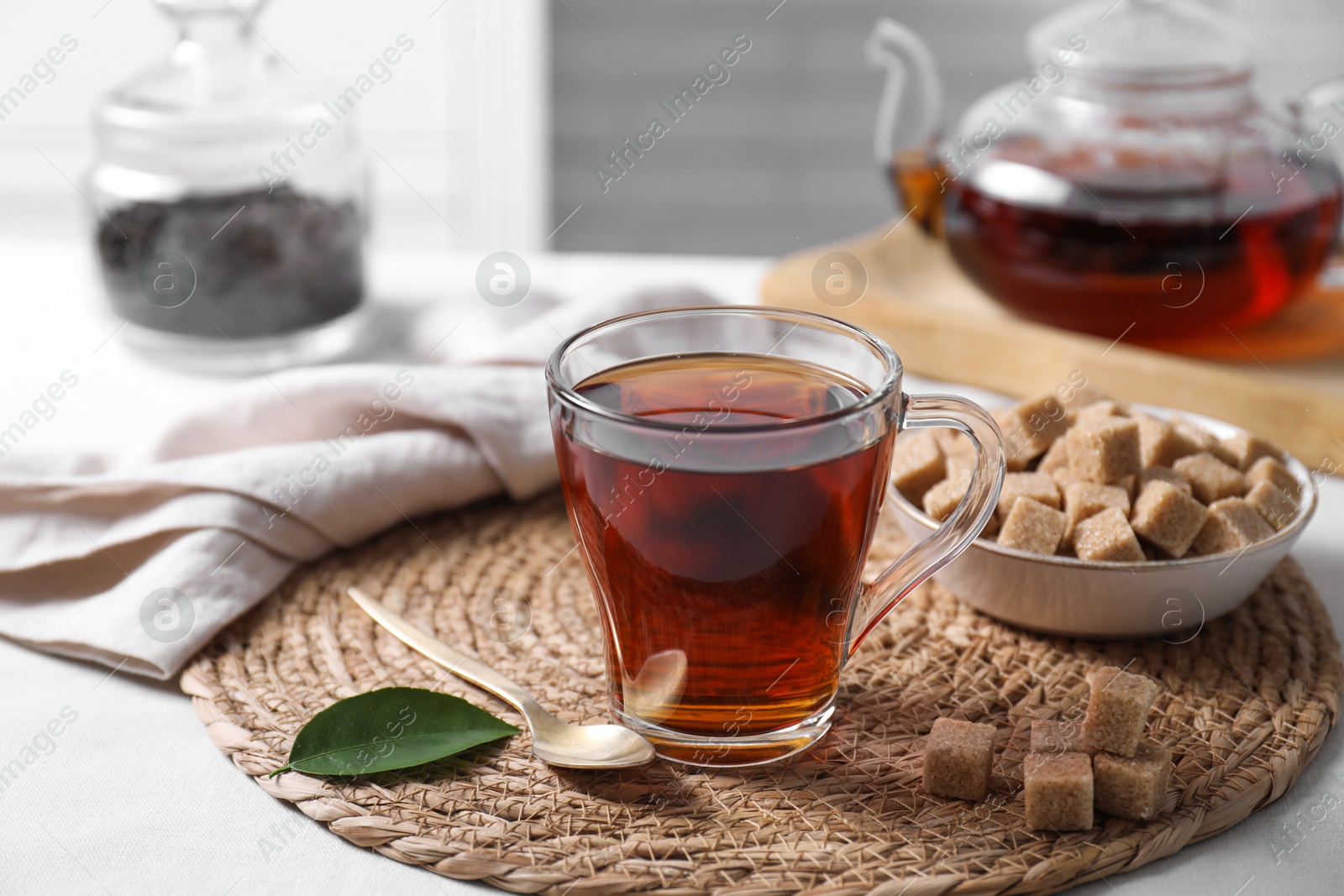 Photo of Aromatic black tea in cup and brown sugar cubes on white table, closeup