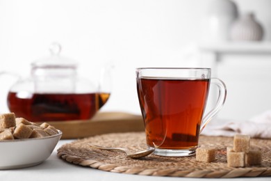 Photo of Aromatic black tea in cup and brown sugar cubes on white table, closeup