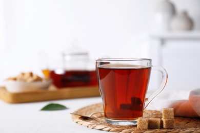 Aromatic black tea in cup and brown sugar cubes on white table, closeup. Space for text