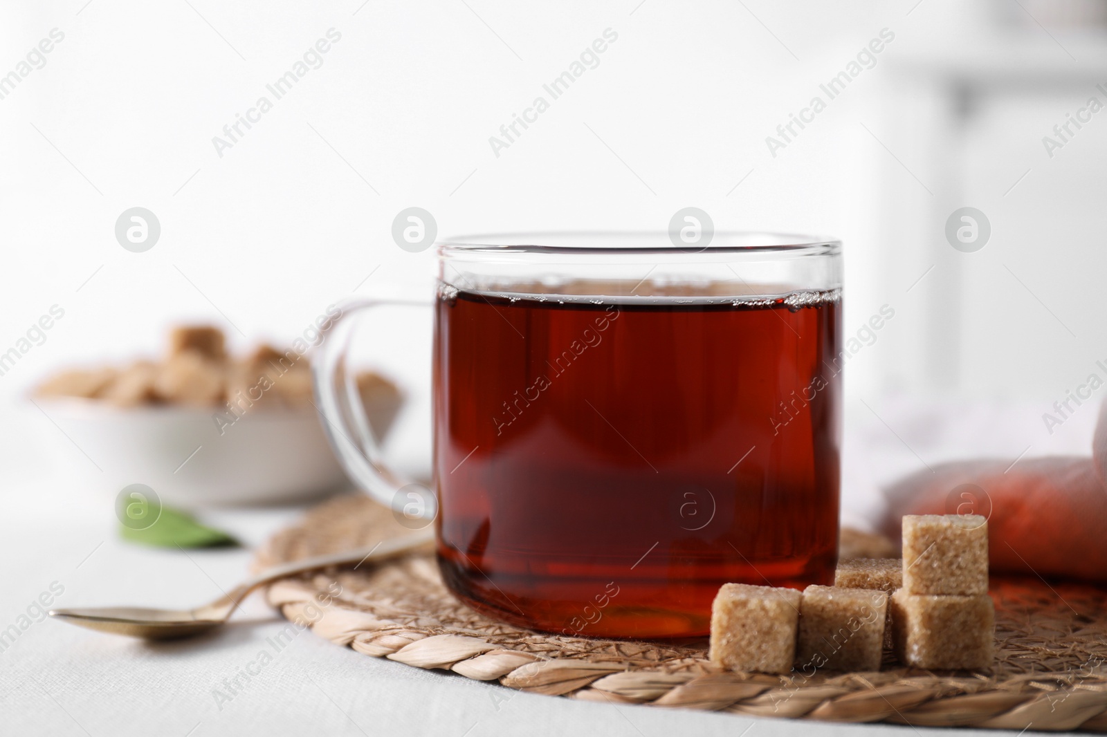 Photo of Aromatic black tea in cup and brown sugar cubes on white table, closeup