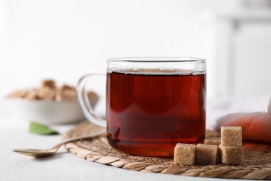 Photo of Aromatic black tea in cup and brown sugar cubes on white table, closeup