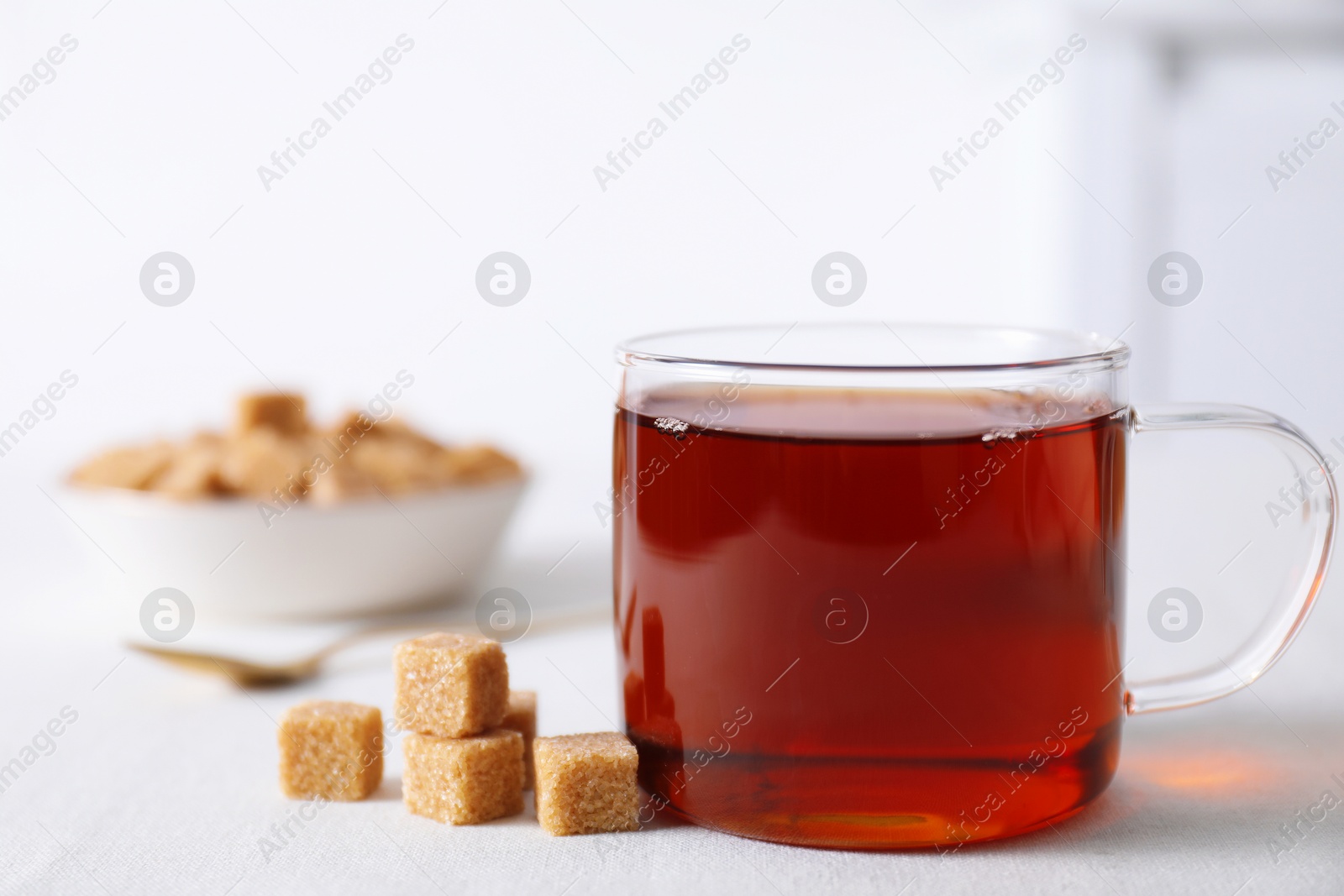 Photo of Aromatic black tea in cup and brown sugar cubes on white table, closeup