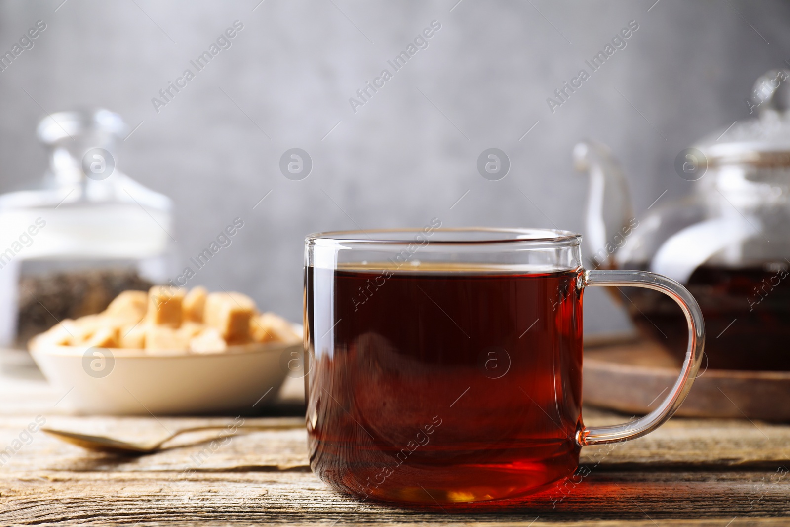 Photo of Aromatic black tea in cup and spoon on wooden table, closeup