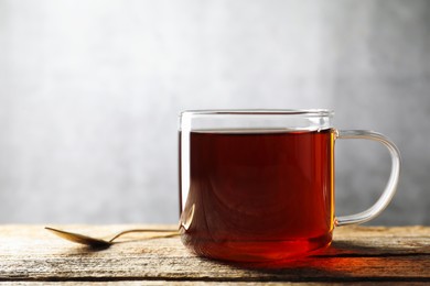 Photo of Aromatic black tea in cup and spoon on wooden table, closeup. Space for text