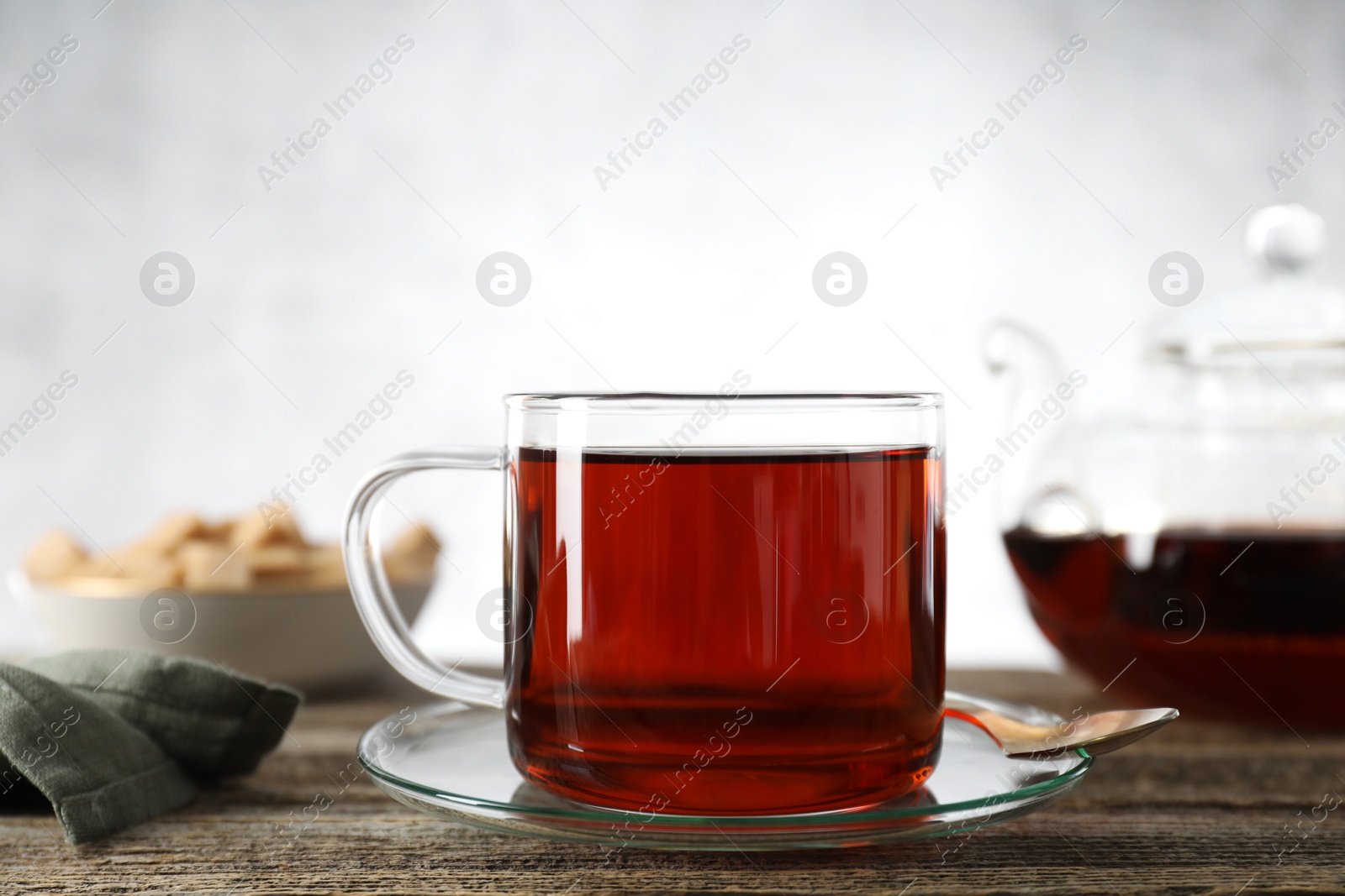 Photo of Aromatic black tea in cup and spoon on wooden table, closeup