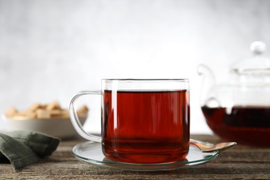 Photo of Aromatic black tea in cup and spoon on wooden table, closeup