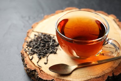 Photo of Aromatic black tea in cup and dry leaves on grey table, closeup