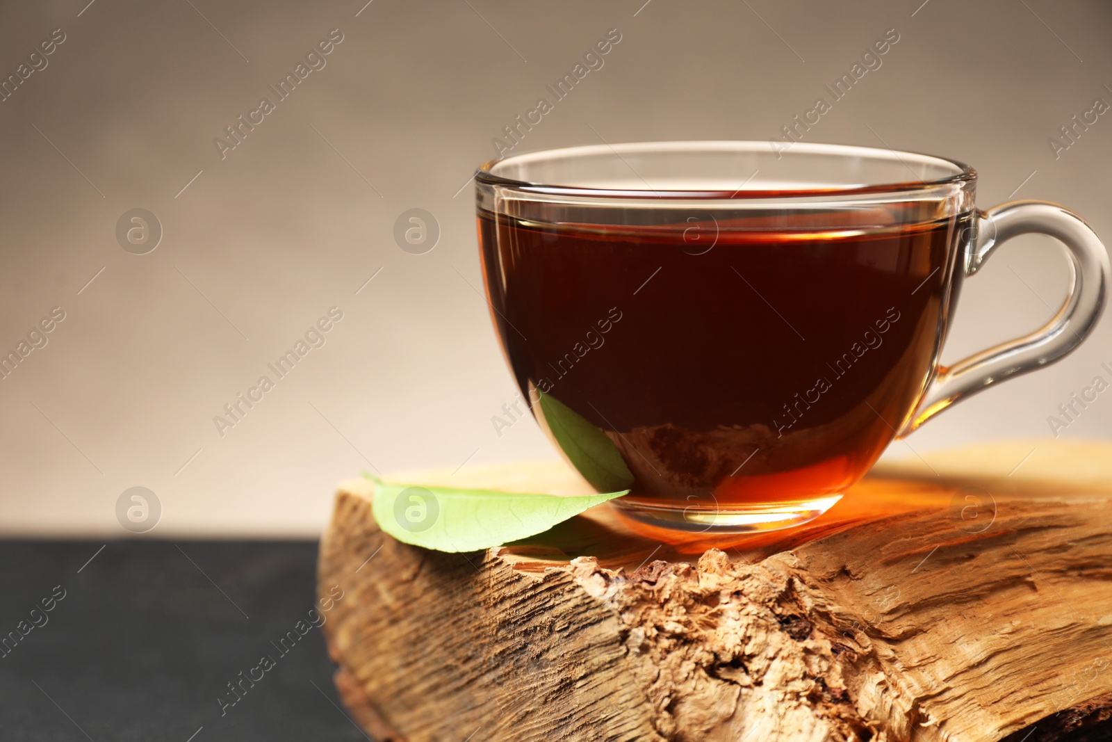 Photo of Aromatic black tea in cup and green leaf on wooden snag, closeup. Space for text