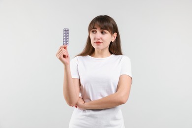 Photo of Young woman with blister of contraceptive pills on light background