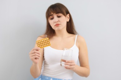 Photo of Upset woman with contraceptive pills and glass of water on light background, selective focus