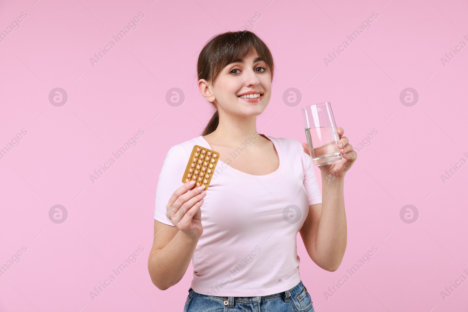 Photo of Smiling woman with contraceptive pills and glass of water on pink background