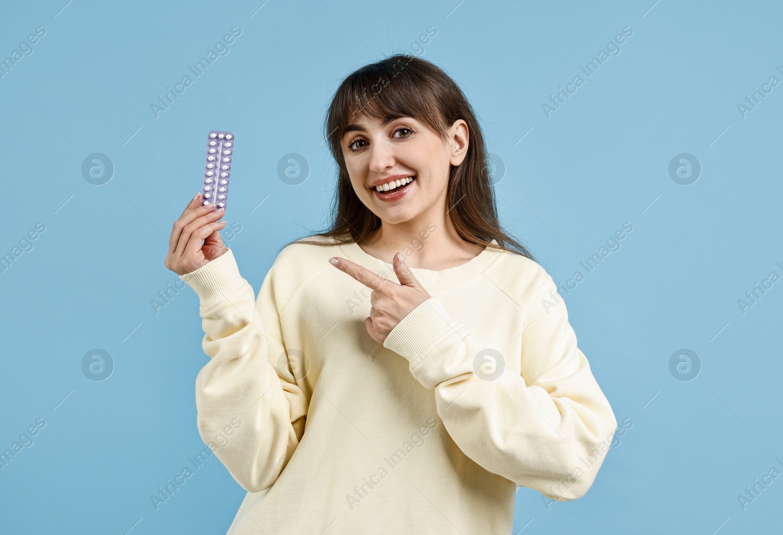 Photo of Smiling woman with blister of contraceptive pills on light blue background